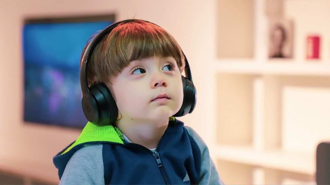 Małe dziecko w sportowej bluzie i w dużych słuchawkach słucha audiobooka storytel