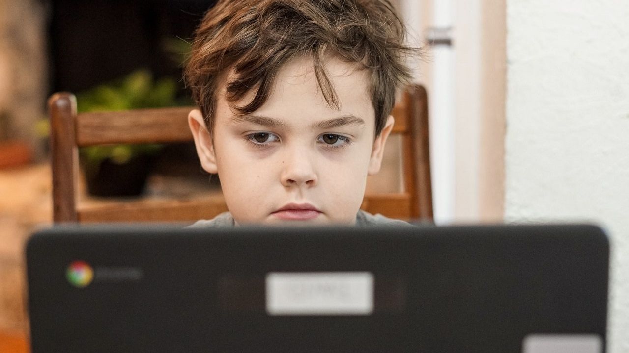 Chłopiec czarne włosy widoczny zza monitora komputera patrzy w ekran słuchając audiobooka storytel