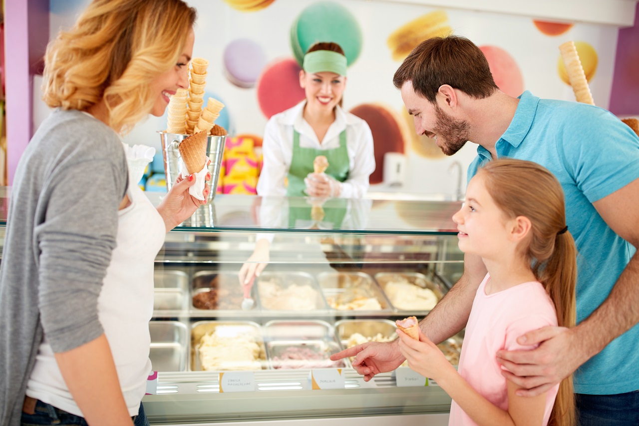 rodzice z dziewczynką w lodziarni kupujący dobre lody naturalne podawane w postaci gałki w wafelku